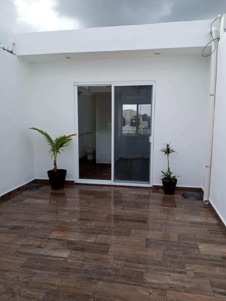 A quiet terrace space features a smooth tiled floor and minimalistic design. Two potted plants are positioned on either side of a glass door, which provides access to the interior. Natural light filters gently through the glass, creating a serene atmosphere.