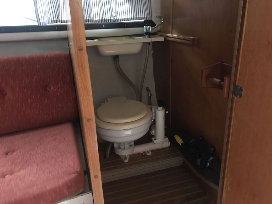 Eenvoudig toilet met sceptic tank, opbergmogelijkheden voor toiletspullen en spiegel.