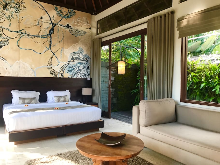 Master bedroom with garden balcony, couch, tv, coffee table, large closet and entrance way to en suite bathroom. Original art.