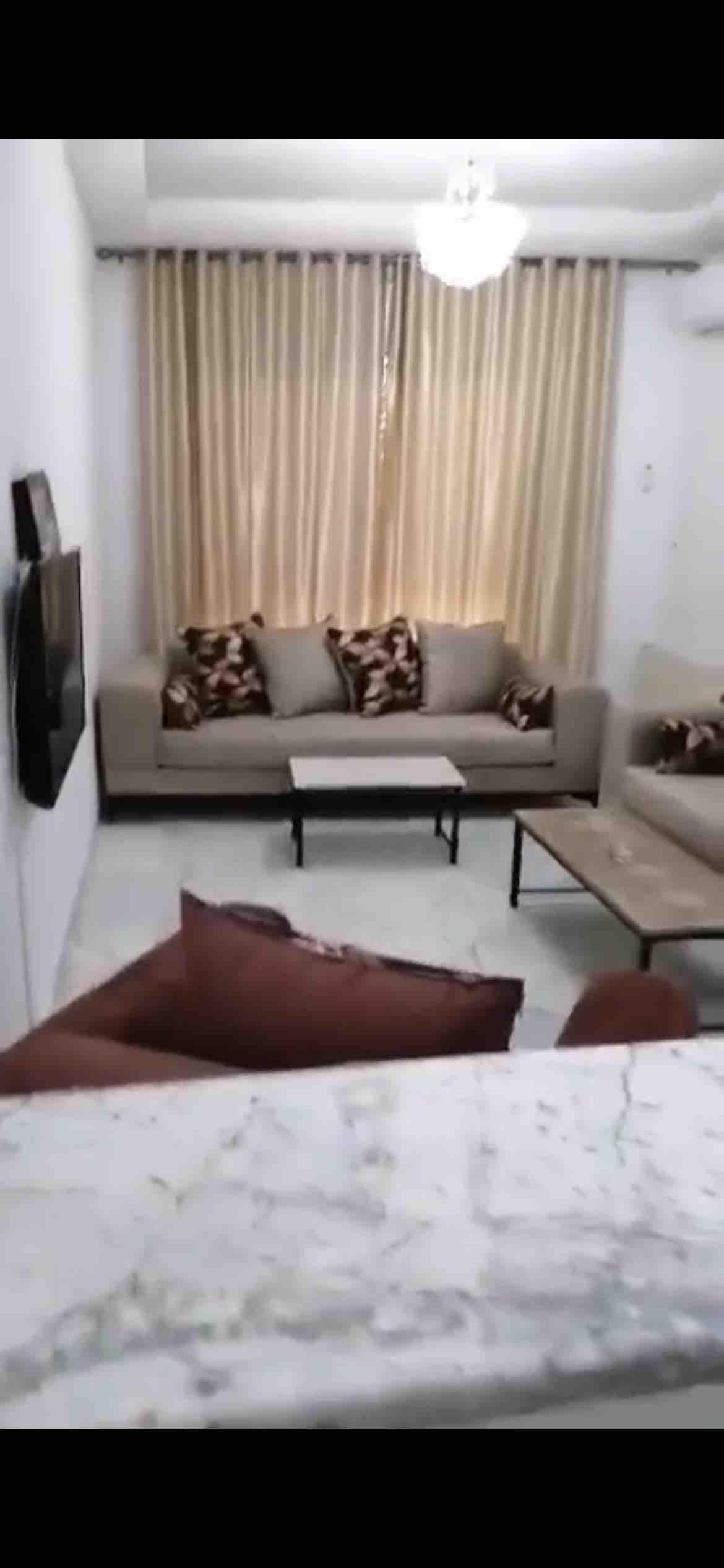 A light-filled living area is presented with two sofas adorned with patterned cushions. A coffee table is centered on a polished floor. Sheer curtains allow soft light to filter in, complementing the neutral color palette and maintaining a calm atmosphere.