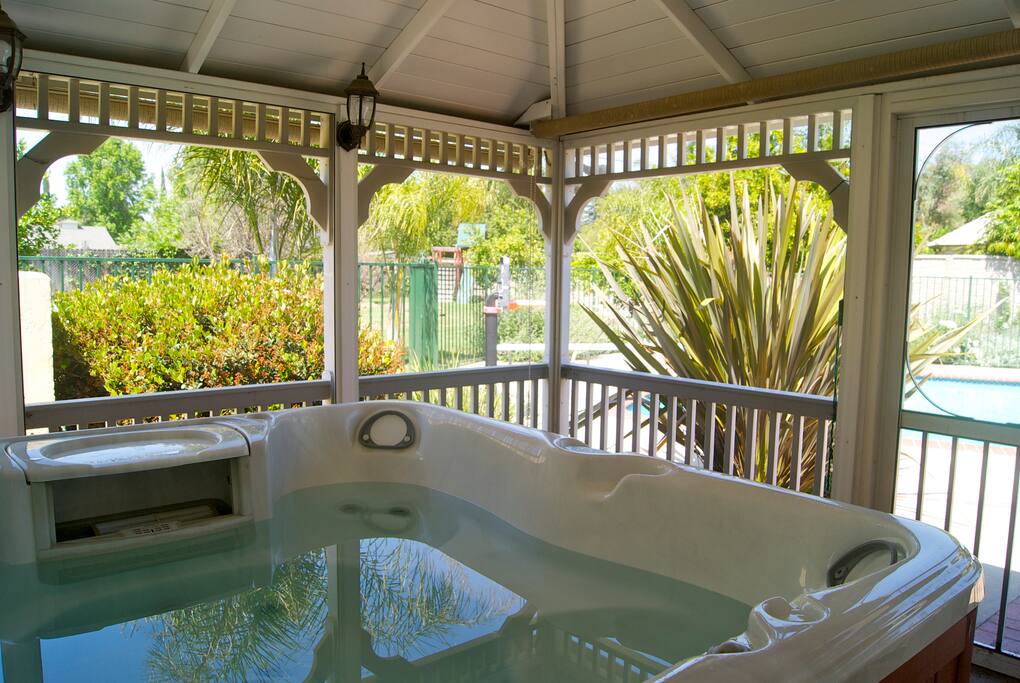 The hot tub is inside of a screened in gazebo.
