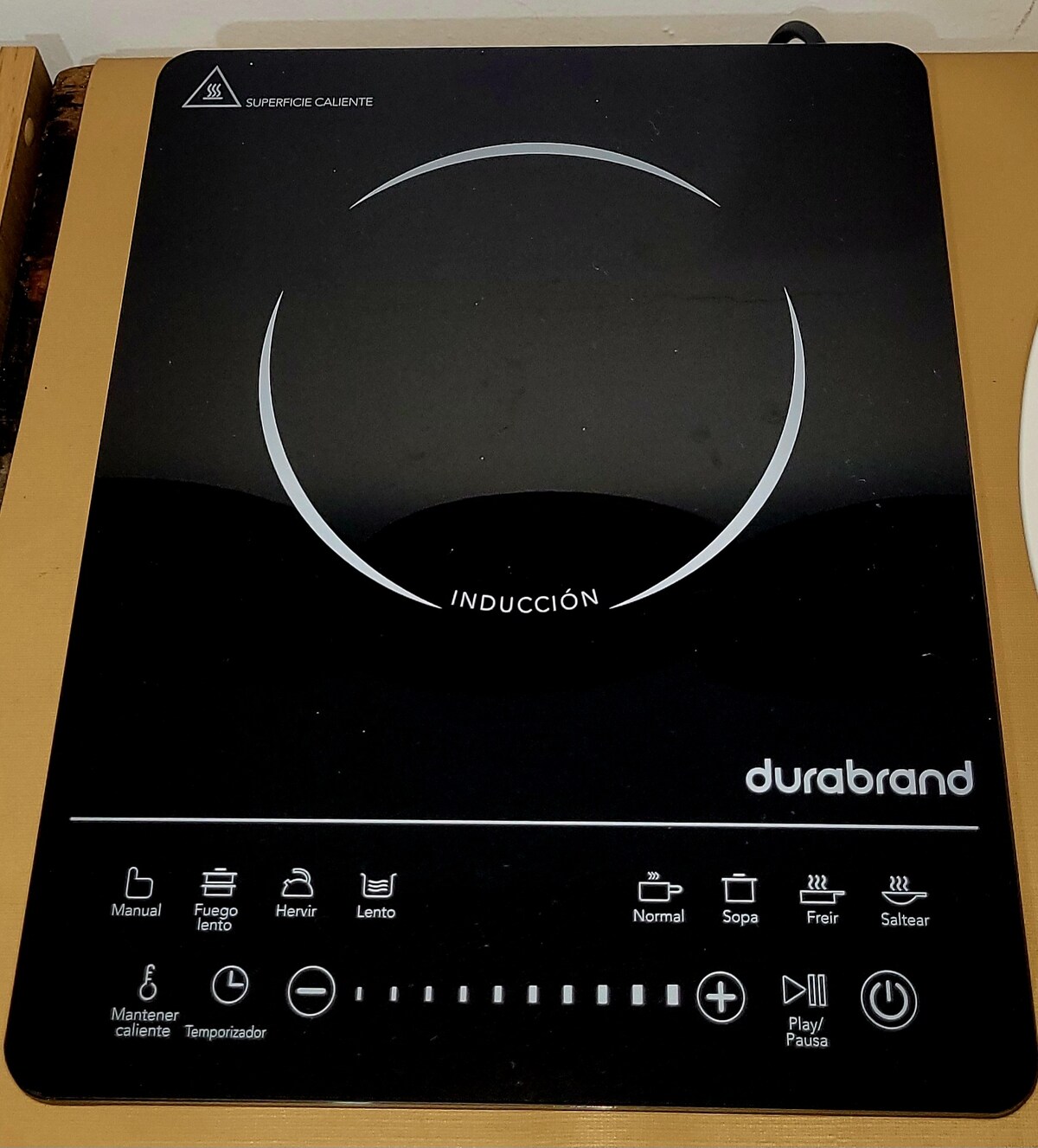 An induction cooktop with a sleek black surface features a circular heating area and clearly labeled control buttons. The minimalist design includes symbols for various cooking functions, ensuring easy temperature adjustments and cooking settings.