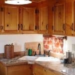 A well-equipped kitchen features wooden cabinets, a spacious countertop, and a rustic backsplash. A farmhouse-style sink is complemented by modern fixtures, while kitchen utensils and appliances are neatly arranged, creating a functional space for meal preparation.