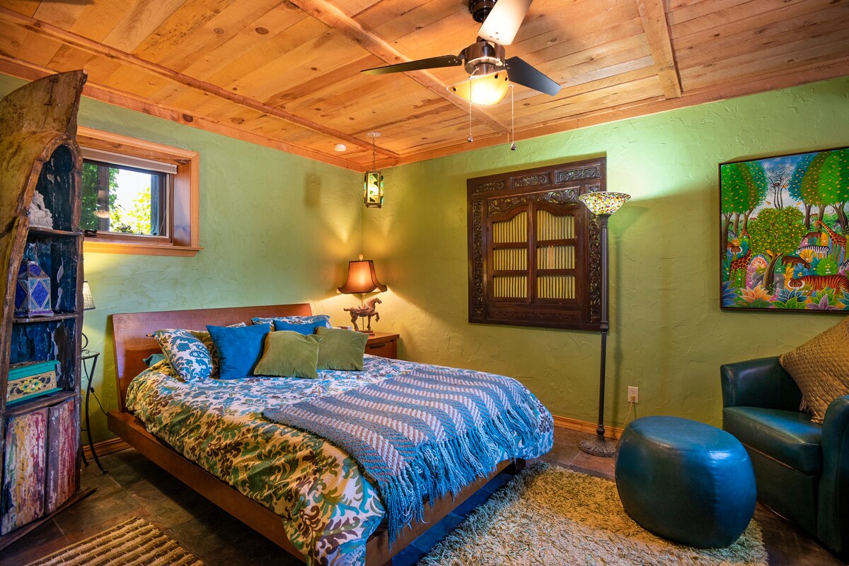 Queensize slaapkamer met een tropisch gevoel. Met een uniek raam dat uitkijkt op een weelderige kas. 