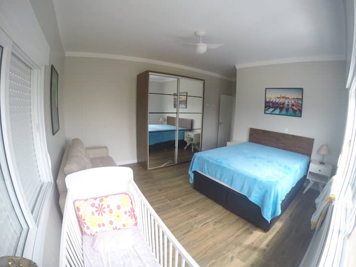 Suite con cama tamaño queen, cuna con ruedas, armario y sofá cama.