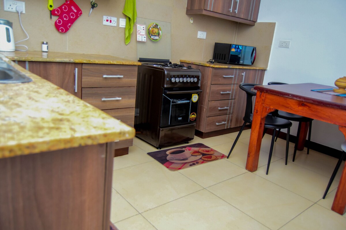 A modern kitchen enhances functionality with dark wooden cabinetry and a granite countertop. Essential appliances, including a gas stove and microwave, are strategically placed. A small dining table with black chairs is visible, accompanied by a colorful rug that adds a touch of warmth.