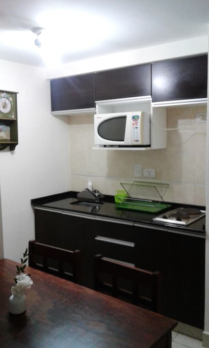 Zona de cocina con microondas, anafe eléctrico, bacha de cocina, heladera, vajilla, etc.