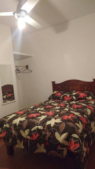 Dormitorio con cama matrimonial, espacio para colgar ropa, cajonera y ventilador de techo.