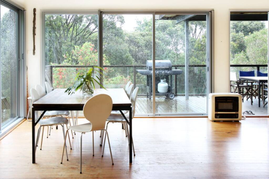 open plan dinning area with large table, leading to deck with BBQ and another matching table.
