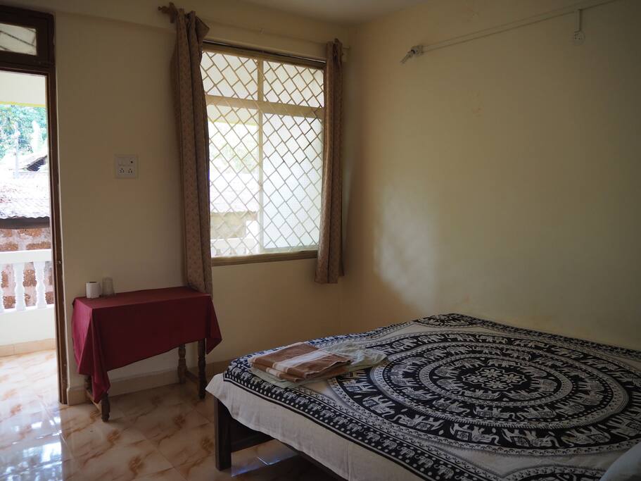 Bright and airy room, furnished with a table, bedside table, lamp and shelf unit