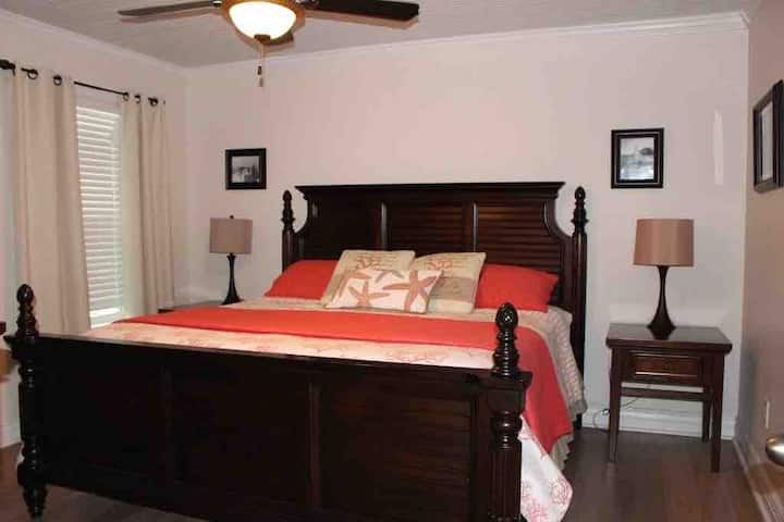 Chambre king size avec salle de bain attenante.  Il est situé en dehors de la cuisine.  Cette chambre possède également sa propre porte qui mène à l'extérieur du porche fermé latéral.  Elle dispose d'un ventilateur de plafond 