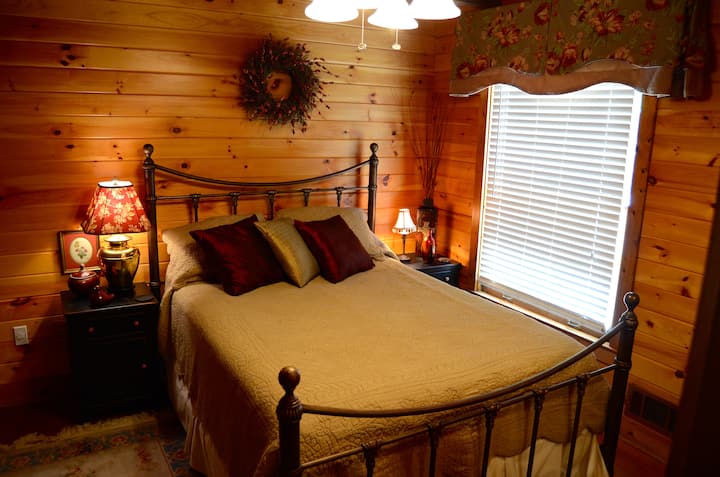 Acogedor dormitorio principal con una cómoda cama tamaño queen y paredes de pino