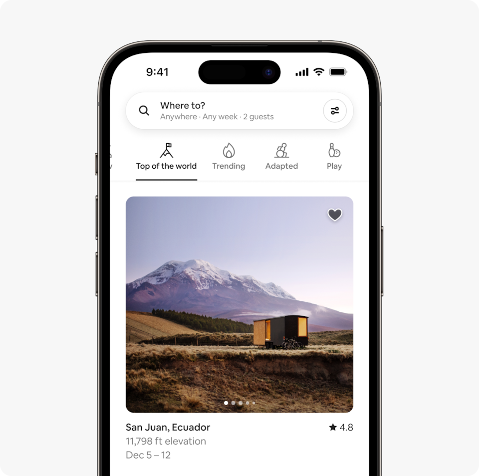 A laptop and a phone show the Airbnb homepage with two rows of homes from a new Airbnb Winter Release category called Top of the World, which features homes at high altitude, around 10,000 feet above sea level.