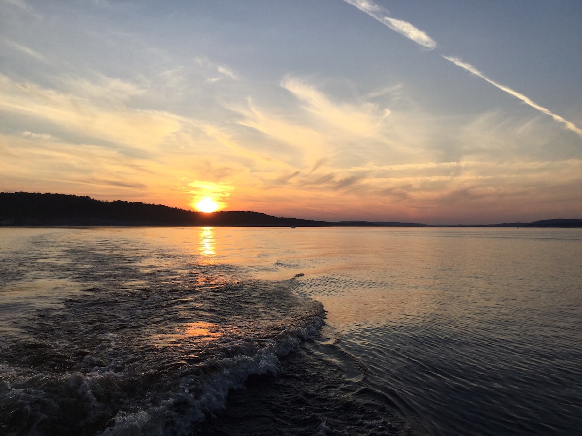 A sunset paints the sky with warm hues as it reflects off the calm waters of Lake Taureau. Gentle ripples are visible on the surface, complementing the serene landscape. The outline of distant hills can be seen in the background, enhancing the tranquil ambiance.