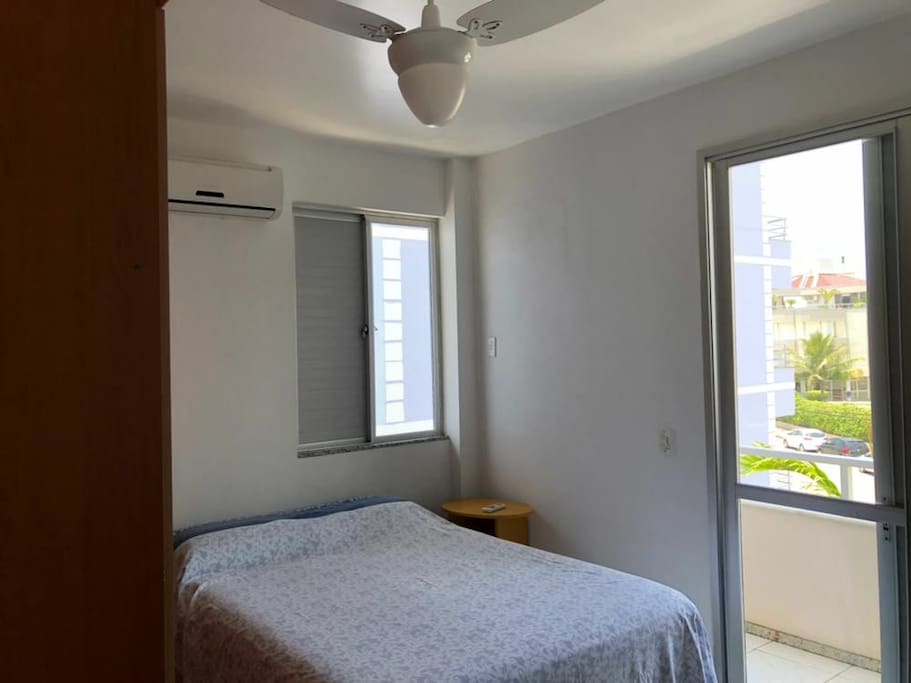 Suíte com sacada, ar condicionado, ventilador, cama de casal e sofá cama.