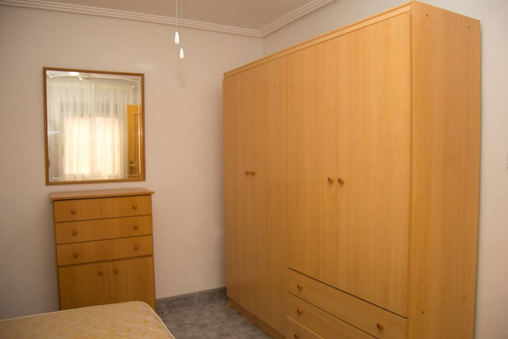 Perspectiva 2 de la habitación con cama de matrimonio. Dos armarios grandes y una cómoda para zapatillas con un espejo y cajones.