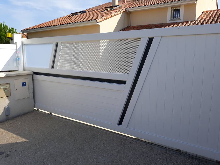 Le portail coulissant blanc aux traits bleu-noirs où se trouve le parking.