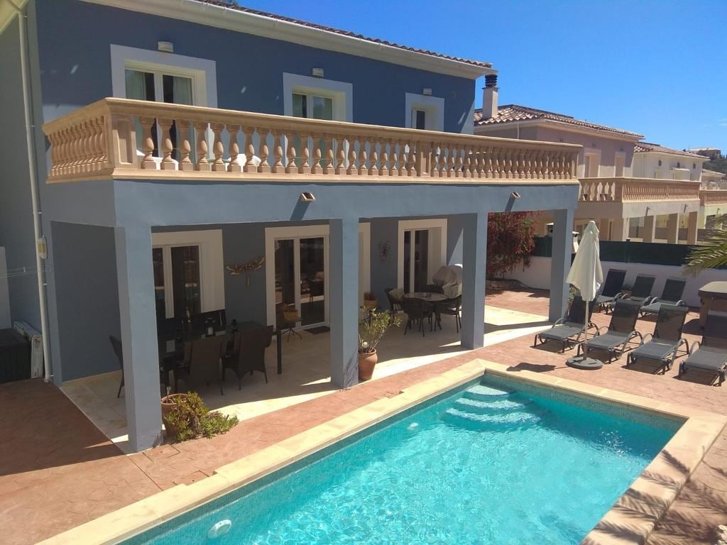 The exterior view reveals a spacious villa featuring a private pool surrounded by loungers. A large terrace is accessible from the upper floor, showcasing a dining area with multiple chairs and tables. The building’s design includes elegant balconies and large windows for ample natural light.