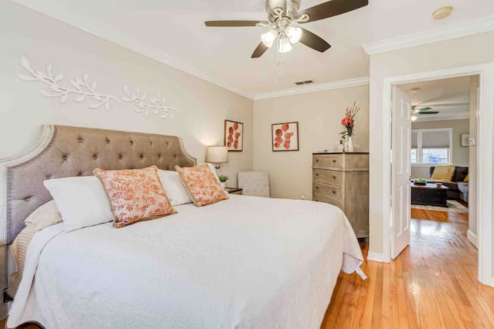 Experience comfort in the well-lit master bedroom with optional blackout blinds, a cozy bed with microfiber bedding, and a ceiling fan. Located off the living room and next to the bathroom, with a sitting area for reading or putting on shoes.