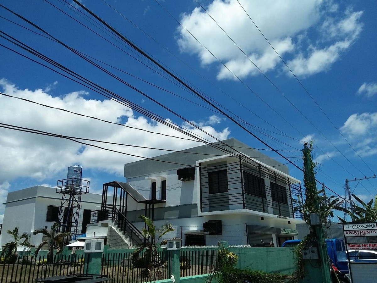 A two-story building is shown with a modern exterior design. The structure features large windows and a staircase leading to the second floor. A clear blue sky with fluffy clouds serves as the backdrop, while utility lines run across the image.