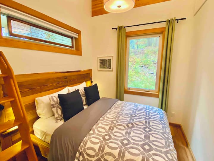 Queen bed with frame made from custom reclaimed oak. Hotel linens and blackout curtains and shade. Stairs access a reading nook.