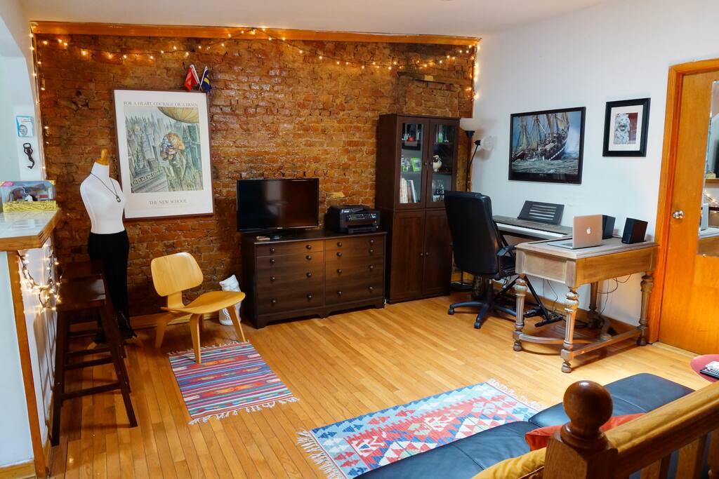 Shared living room area has a couch, an Eames chair, TV and a keyboard. Nicely lit from the kitchen windows, and the sky light.