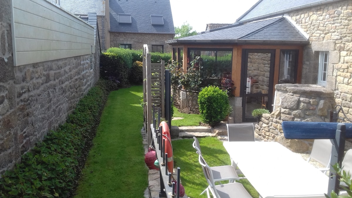 A well-maintained garden area is visible, featuring a neatly trimmed lawn bordered by stone walls and greenery. A terrace with outdoor furniture is seen, along with a gazebo that offers a shaded seating area. Pathways lead through the tranquil outdoor space.