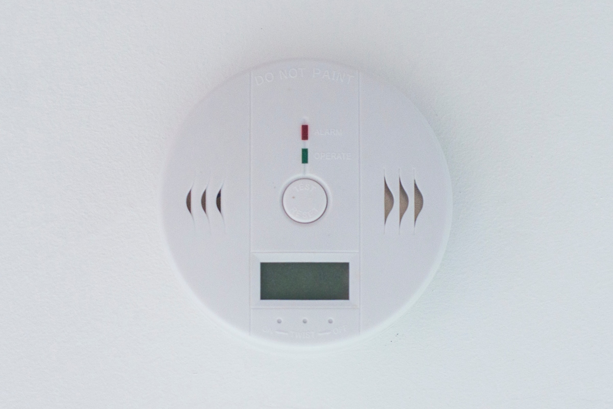 A smoke detector is mounted on the ceiling, featuring lights that indicate alarm and power status. A circular design with vents is visible, ensuring safety within the space.