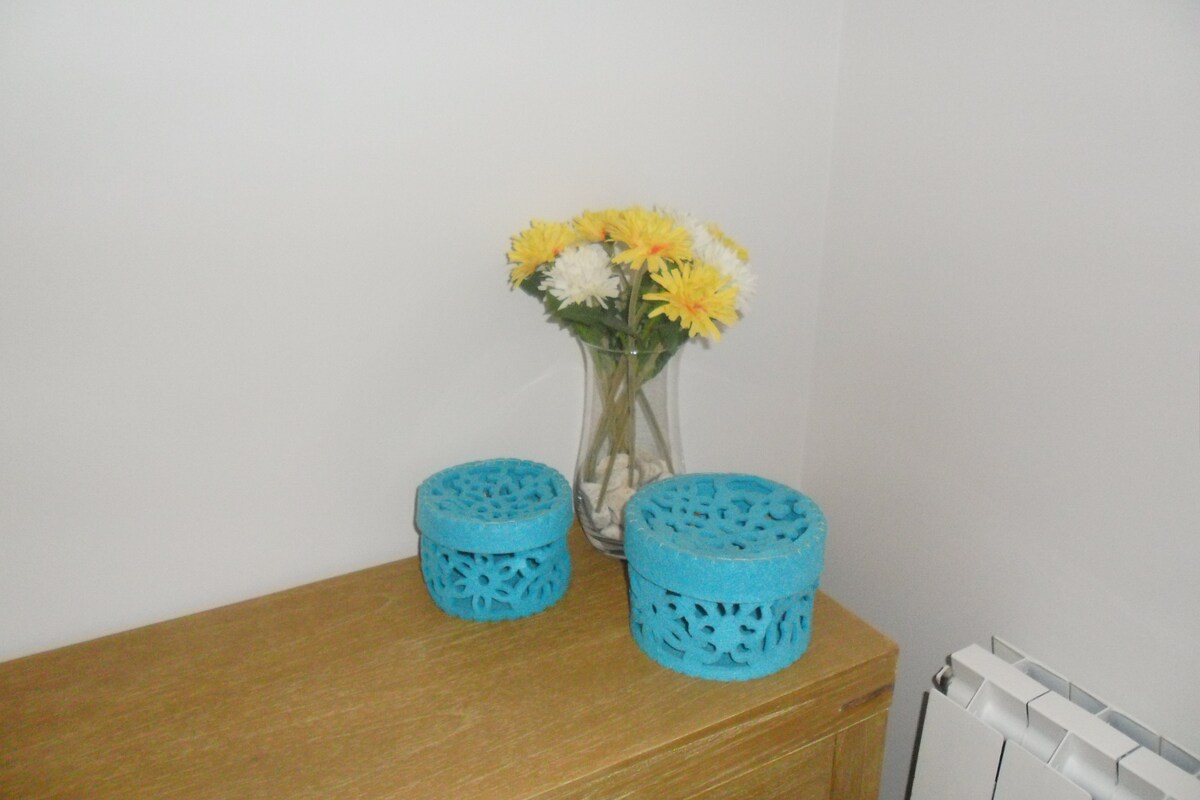 A wooden surface displays two turquoise containers with intricate cut-out patterns, along with a glass vase filled with bright yellow and white flowers. The simplicity of the arrangement contributes to a calming aesthetic.