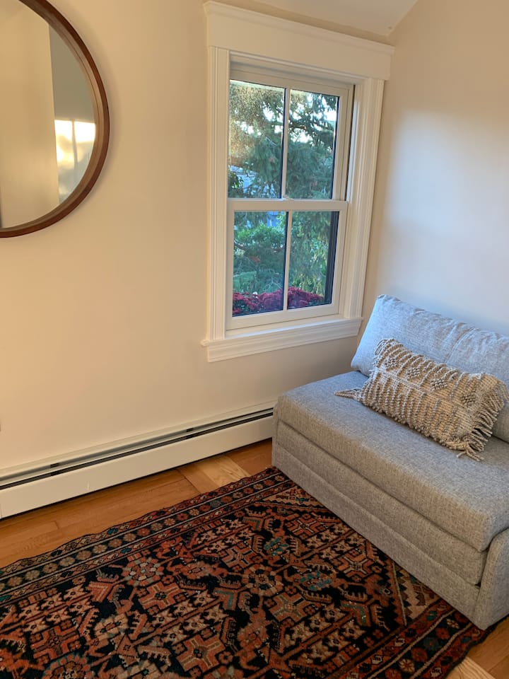 Këndi i lezetshëm i leximit në dhomën e gjumit të dytë me një divan që tërhiqet në një krevat dopio 