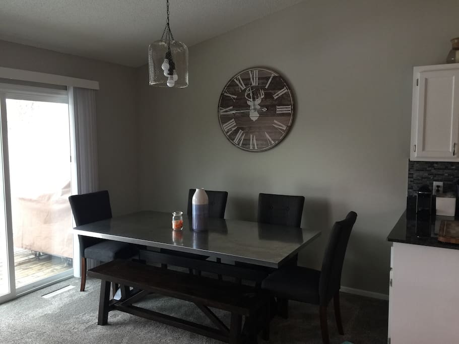 Dinning room table is stainless top with four chairs and a bench. Dimmable light above.