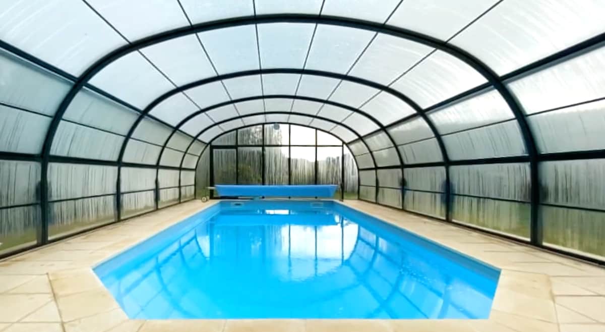 An indoor pool is enclosed within a spacious frame, allowing plenty of natural light to flood the area. The water reflects a calming blue shade, while the surrounding tiles provide a clean, smooth surface. Transparent panels offer views of the outdoor landscape.