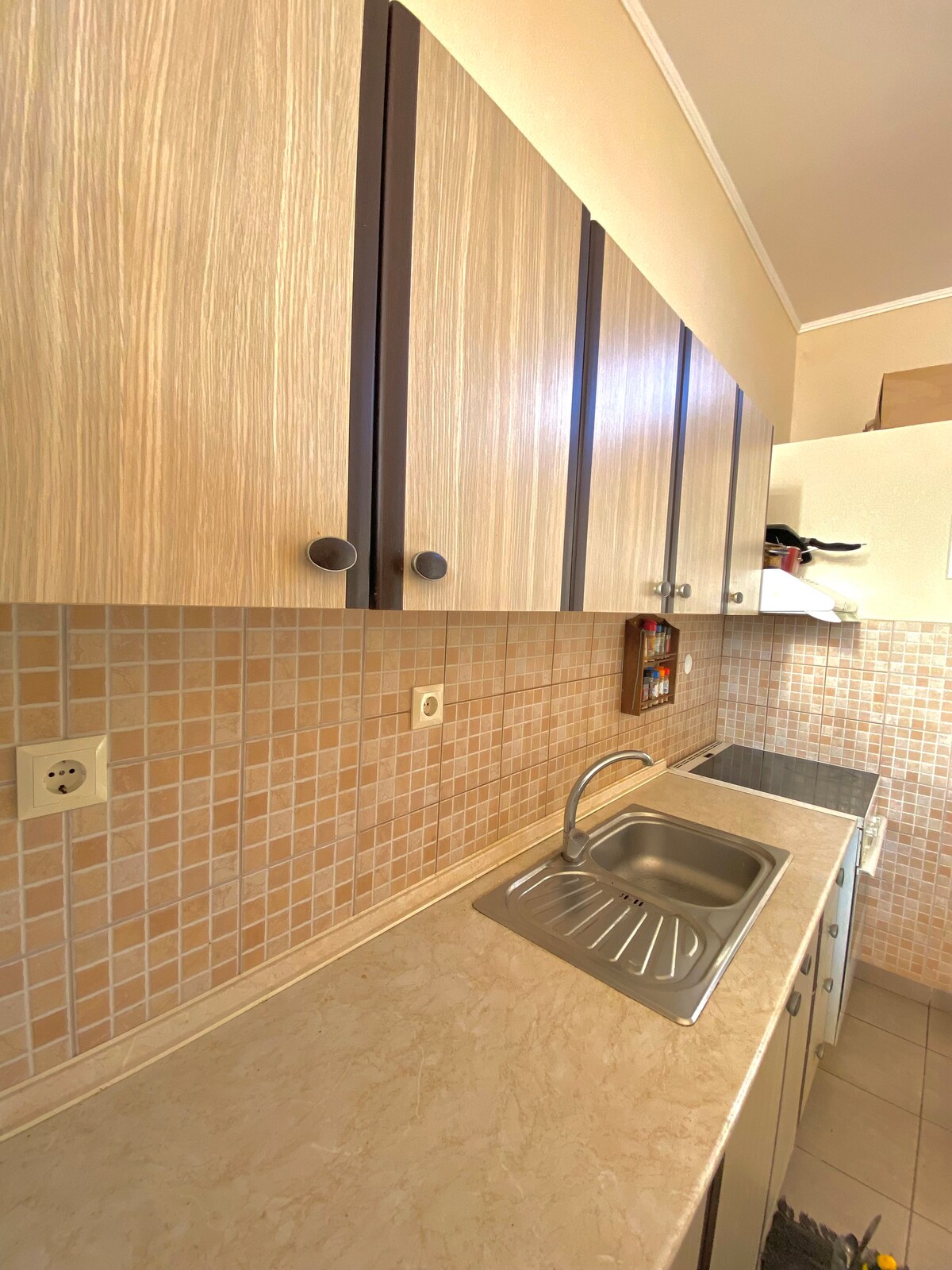 The kitchen is equipped with light-colored cabinets featuring simple handles. A stainless steel sink is positioned on a smooth countertop, with a tiled backsplash in neutral tones adding a clean look. Additional appliances and storage can be seen within the space.