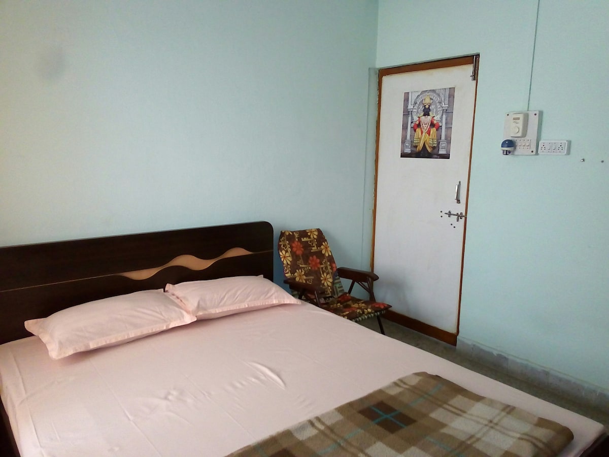 The private room features a spacious bed adorned with soft bedding. A comfortable chair is positioned near the door, which is decorated with a poster. The walls are painted in a calming light blue, complementing the neutral tones of the room.