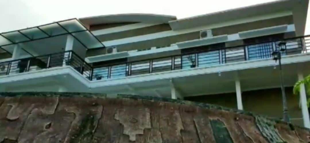 The exterior of a multi-level villa is visible, showcasing a modern design. Expansive balconies are present on each floor, with railings providing a panoramic view. Air conditioning units are mounted on the walls, and large windows enhance the natural light throughout the structure.