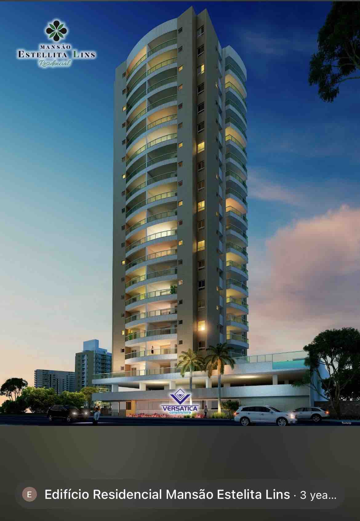 A modern high-rise building stands tall against a dusky sky. The structure features a sleek design with large curved balconies and glass facades. The entrance area is visible, showcasing a well-lit ground floor and landscaped surroundings.
