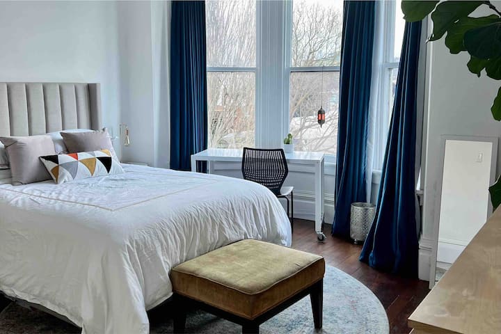 Dormitorio 1 con cama queen, cajonera, perchero y mesa y silla. Mucha luz orientada a la calle con cortinas oscurecidas.