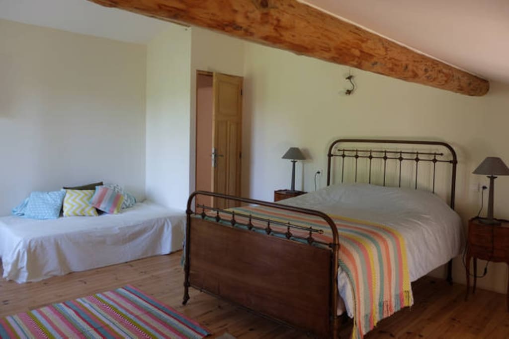 Chambre spacieuse avec poutre apparente, calme et lumineuse. Elle est équipée de : 1 lit double, 1 lit simple, une étagère, un bureau, 1 penderie.