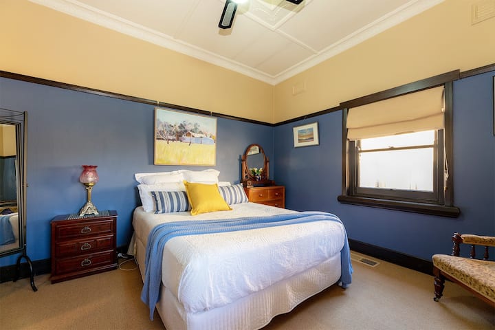 An elegant and spacious bedroom features a Queen bed with linen, a rustic bed-side table and a timber vanity