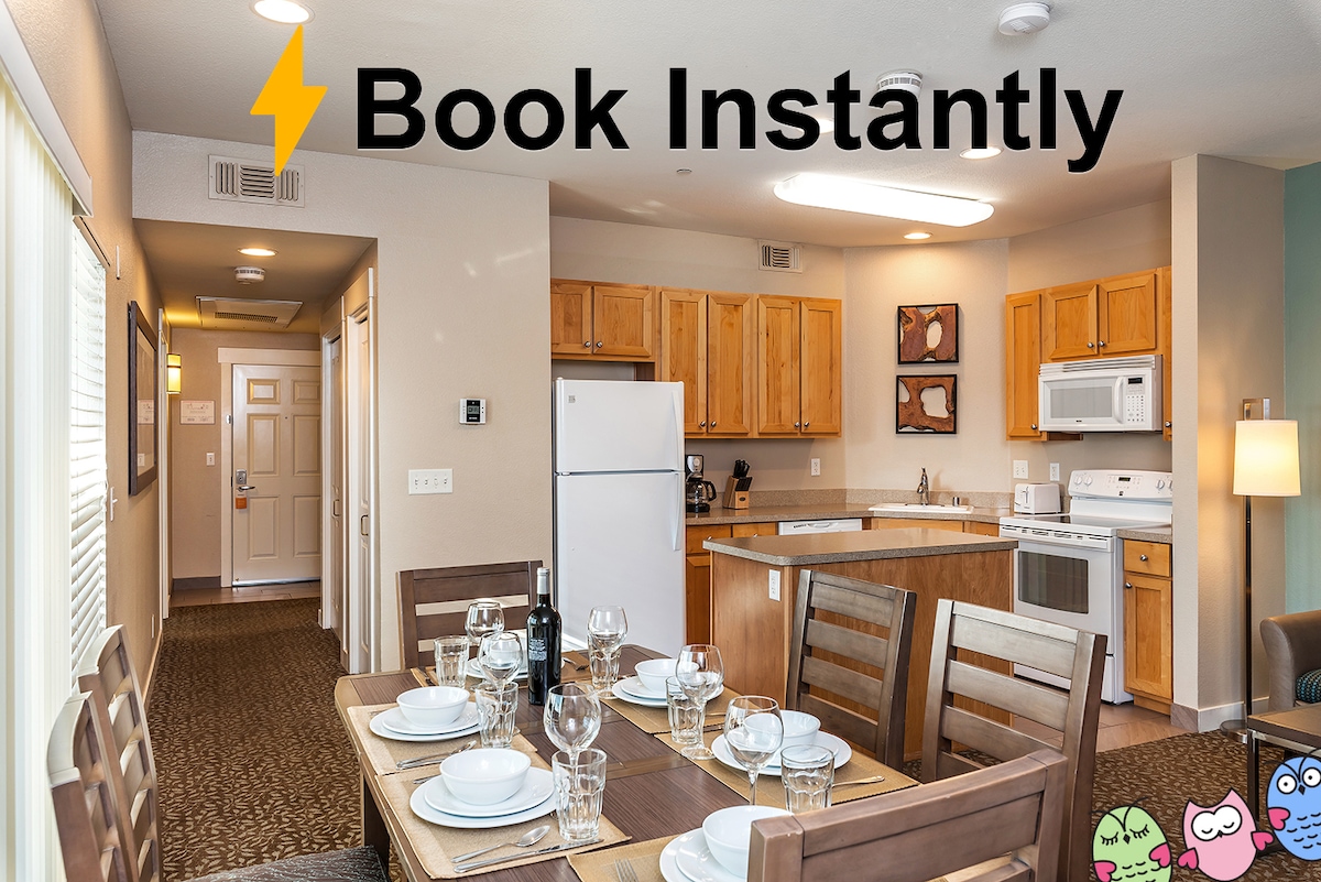 A well-equipped kitchen and dining area are featured, showcasing wooden cabinetry and a large dining table set for six. Modern appliances include a refrigerator, stove, and microwave. Natural light floods the space through a window, creating a bright and functional atmosphere.