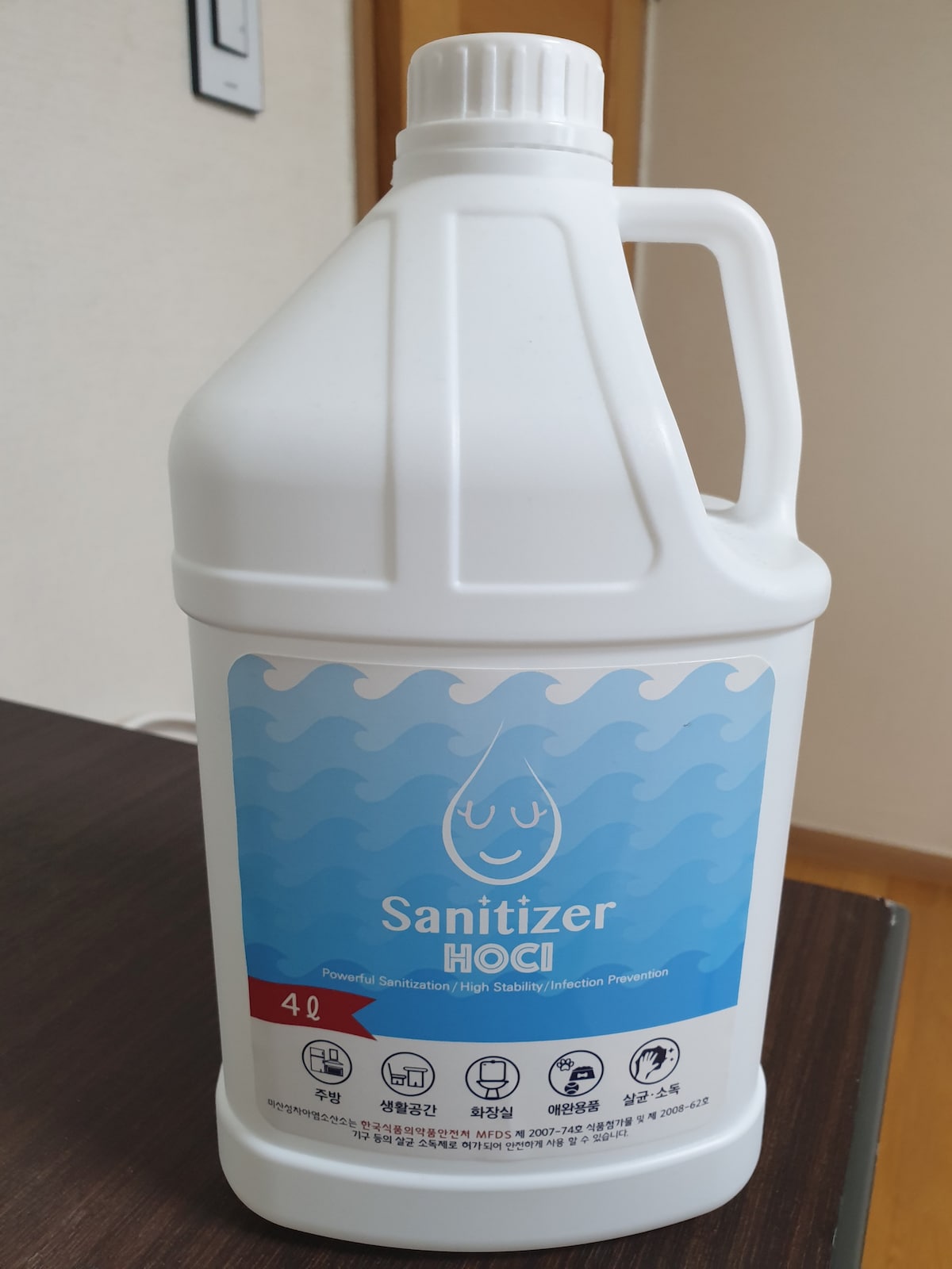A large white bottle of sanitizer is displayed on a wooden surface. The bottle features a colorful label, indicating it is a powerful sanitizer with high stability and infection prevention attributes. The volume of the bottle is noted as 4 liters.