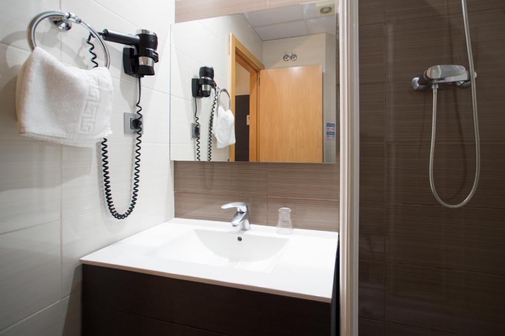 A well-appointed bathroom features a modern sink with a sleek faucet and a wall-mounted hairdryer. Towel racks hold neatly arranged towels, while full-length mirrors reflect light, enhancing the space. A walk-in shower is visible, enclosed by glass panels.