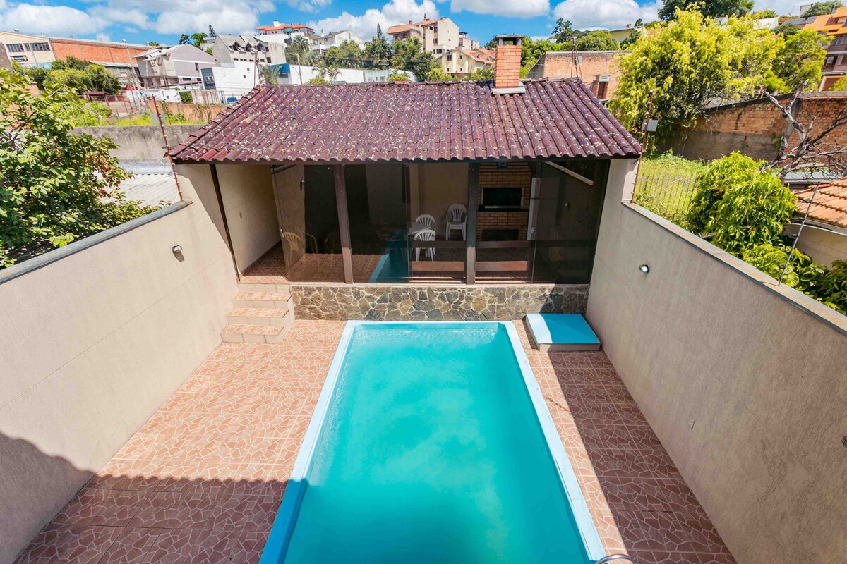 An outdoor area is highlighted by a rectangular swimming pool, surrounded by a tiled deck. A covered patio with a barrel-shaped roof features a built-in barbecue grill and seating, providing a shaded space for relaxation. Lush greenery and nearby structures create a sense of privacy.