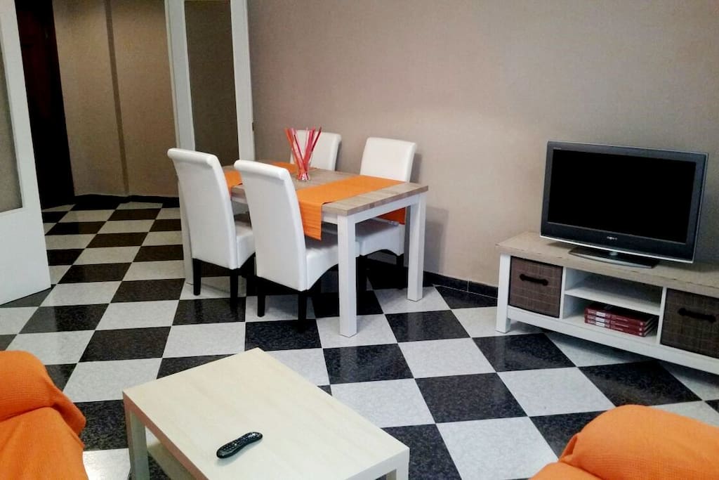 Salón con dos sofás, mesa comedor alta, gran televisor y salida a terraza. 2° foto