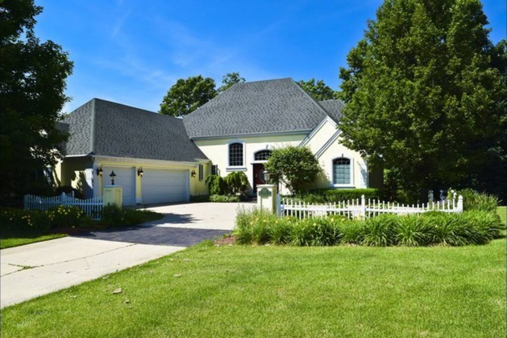 Waterfront large home driveway view with pontoon boat, fire pit lawn chairs, kayaks, and ping pong table and more!