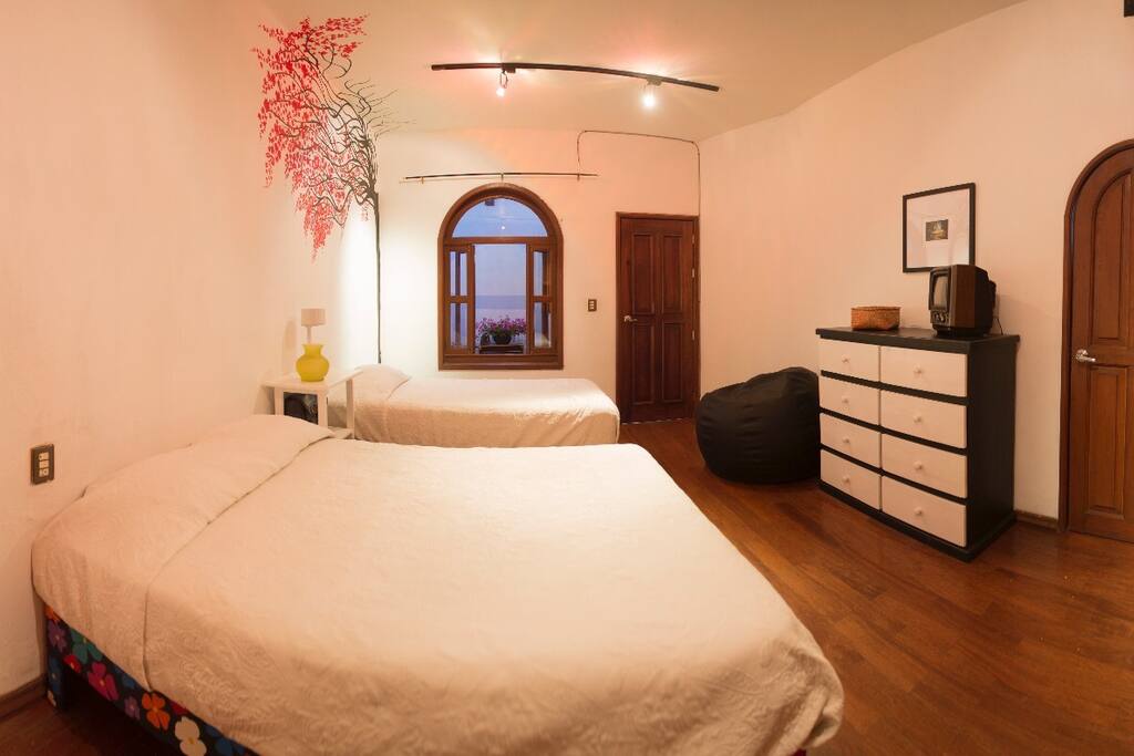 Esta es la "Habitación Cerezos", una de las 3 recámaras en renta de la "Casa la Negra", cuenta con una cama matrimonial, una individual y una hamaca. Además de cómoda y clóset para acomodar la ropa y un escritorio para poder trabajar de manera privada. Tiene baño completo exclusivo y la posibilidad de usar espacio en la cochera para un vehículo.