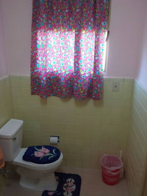 Este es el lado derecho del baño el cual tiene una ventana con cortina para más privacidad y una taza de inodoro con una manguerita manual.