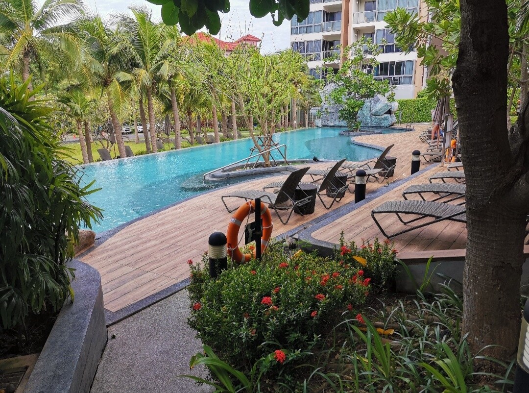 A serene outdoor pool area features a winding swimming pool surrounded by palm trees and tropical foliage. Lounge chairs are arranged along the poolside, inviting relaxation. Beautifully landscaped gardens with vibrant flowers enhance the natural setting, creating a tranquil environment for guests.