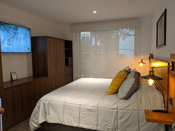 Dormitorio principal con cama tamaño king, TV inteligente, Netflix, lámparas regulables junto a la cama, armario, baño, persianas con blackout y vista a la calle.