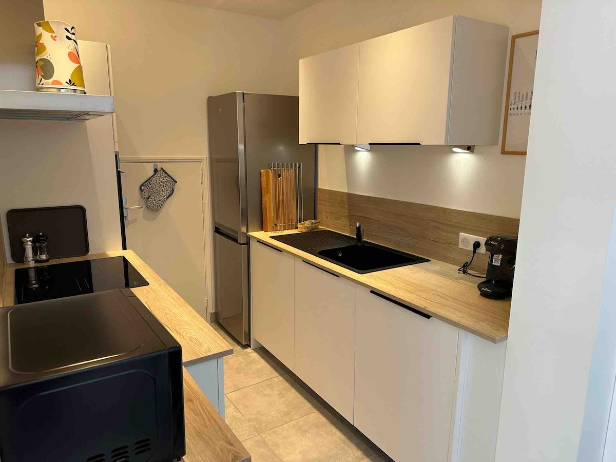The modern kitchen displays sleek cabinetry and a minimalist design. It features a dark sink and countertop, complemented by stainless steel appliances including a refrigerator and coffee maker. Task lighting is provided under the cabinets, enhancing the workspace.